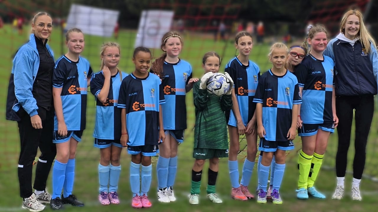 A St Neots Town FC girls' youth team in Torque DMS sponsored kit, pictured on the pitch with their coaches
